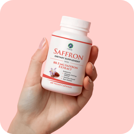 A hand holding a white bottle of Saffron dietary supplement with a white cap, set against a solid light pink background.